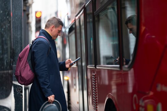 Man checking phone near red bus