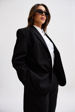 Woman in black suit and sunglasses poses for a studio shot