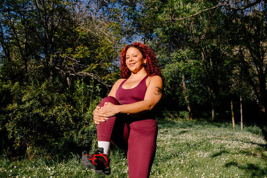 A confident curvy woman completing pre-exercise stretches in a park