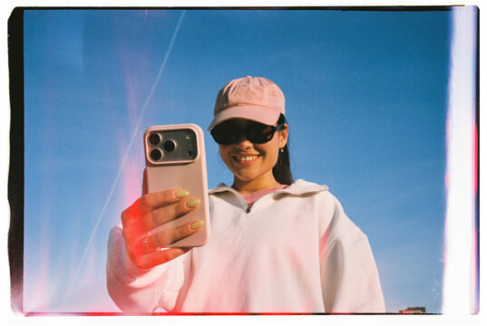 Smiling Woman Using Smartphone Against Blue Sky