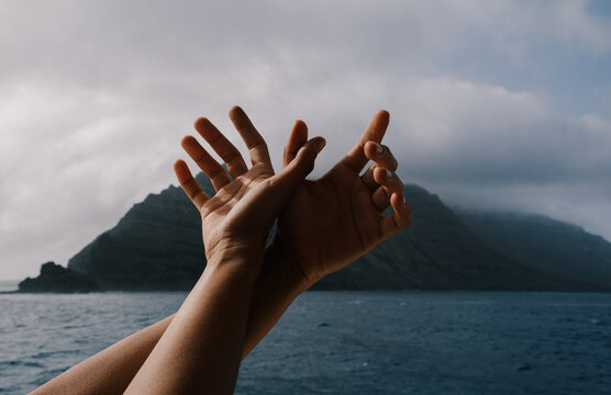 Hands reaching out toward the ocean and mountains 