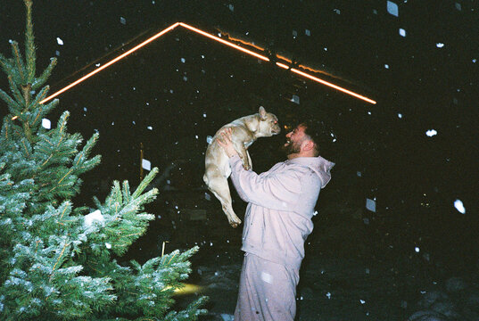 Man lifting French bulldog outside in snow at night
