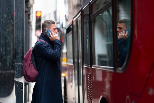 Man talking on phone next to red bus