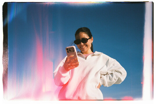Smiling Woman Using Smartphone Against Blue Sky