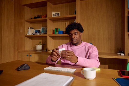 Man is sitting at a desk, holding a pair of wireless earphones