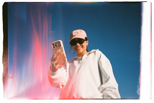 Smiling Woman Using Smartphone Against Blue Sky