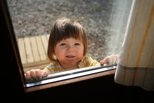 Child Looking Through a Window While Smiling During Daytime
