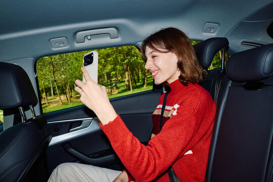 Joyful woman engages with her phone in the backseat of a car
