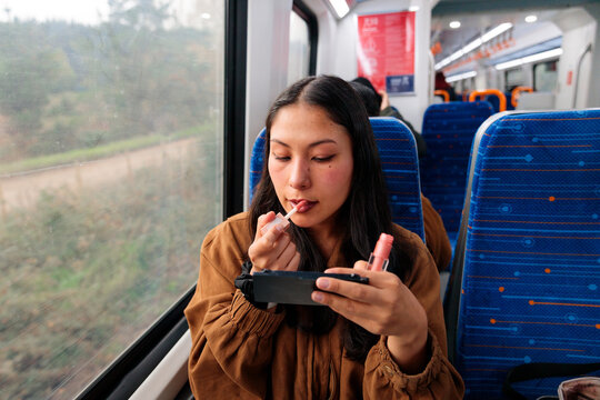 Female commuter applying lip gloss on train