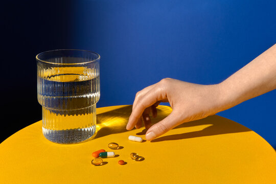 Hand Reaching for Pills Near a Glass of Water on a Table