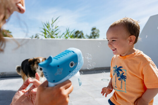 Cheerful toddler playing with bubbles outdoors with dog