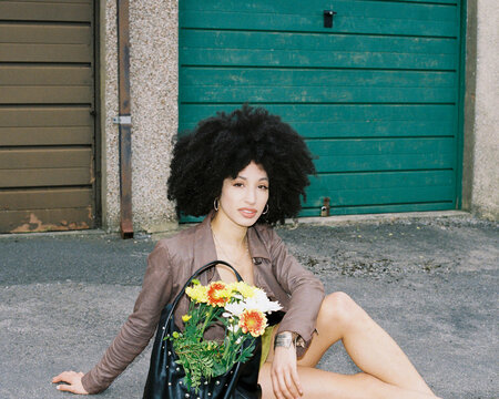 woman with afro sitting on the floor with a bag of flowers on floor