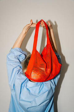 Woman holding bright mesh bag from behind