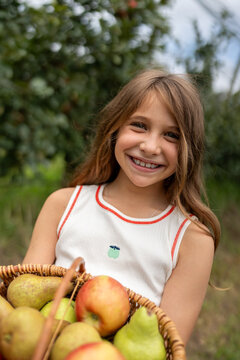 Smiling child carrying basket of fresh orchard fruit