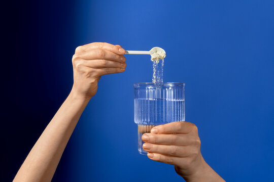 Hands adding white powder supplement into water with a measuring scoop
