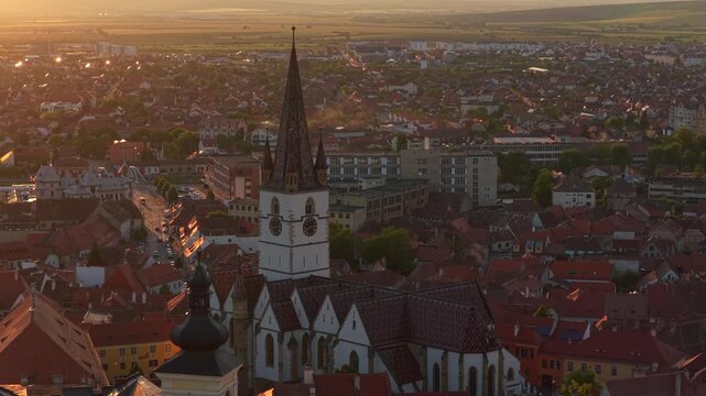 Aerial 4k video of the old town of Sibiu featuring historic red roofs and the tall church tower, with the majestic blue Fagaras mountains visible on the horizon. Sibiu, Transylvania, sunset landscape.