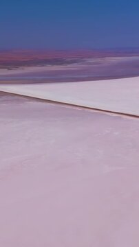 Vertical video. Aksaray, Turkey. Tuz Golu salt works, geometric pink evaporation ponds and straight service roads on a vast white salt flat, aerial drone view under clear blue sky. Aerial View. Rich 