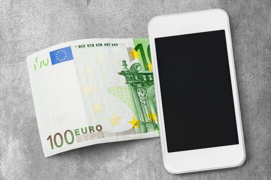 Euro banknote and white smartphone lying on a grey stone surface for mobile payment