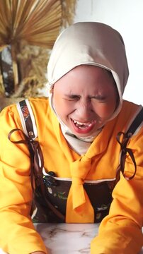A Muslim woman breaking character, wincing and laughing from sudden discomfort.