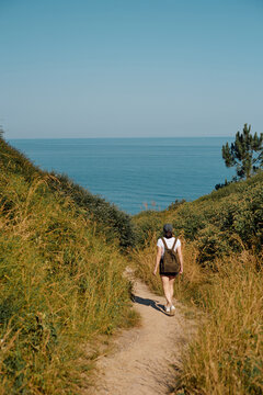 Woman with backpack walking on a coastal path towards the sea