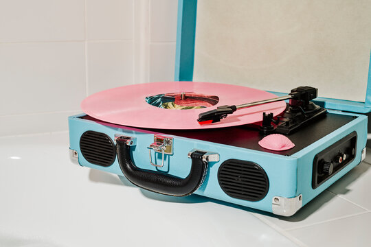 a blue suitcase turntable with a pink vinyl sits on a bathtub edge