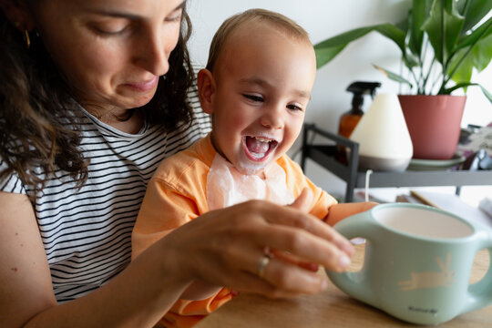 Mother and toddler laughing enjoying messy milk moment
