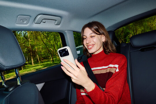 Happy woman uses her phone in the backseat of a car