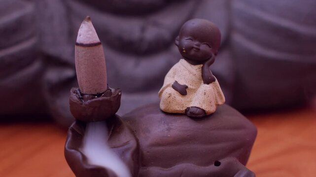 Recreation scent burner. Meditation tool. Fume waterfall stream down in holder with baby monk statue during spiritual yoga session.