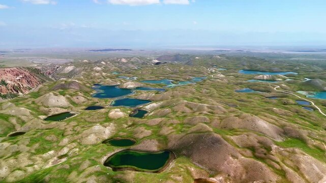 Aerial view of Tulpar Lake and numerous small alpine lakes scattered across rolling green hills under a clear sky in Alay District, Osh Region, Kyrgyzstan.