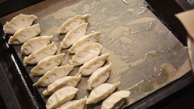 Professional chef neatly arranging raw homemade japanese gyoza on an oiled baking tray. Traditional asian dumplings ready for cooking