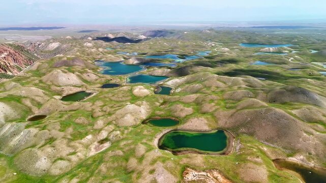 Aerial view of Tulpar Lake featuring turquoise alpine waters nestled among rolling green hills and rugged mountain peaks in Alay District, Osh Region, Kyrgyzstan.