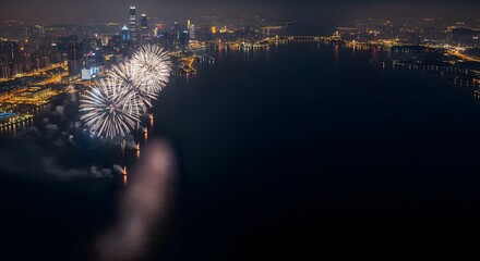 Fototapeta na wymiar Aerial view of bright fireworks over a city skyline at night by the water