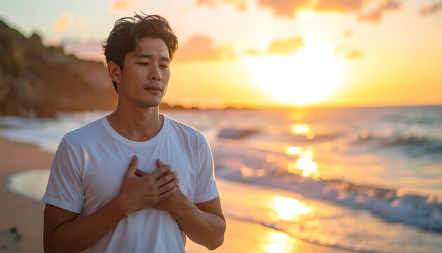 A young man standing on a beach at sunset with his hands on his chest