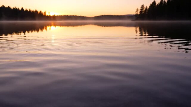 Sunrise over a calm forest lake with a mirror reflection of evergreen silhouettes, morning mist, and a slight ripple on the water surface under a clear orange and purple sky.