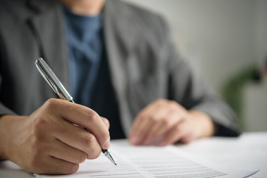 Corporate executive lifestyle showing business person using pen writing on paper form evaluating legal employment contract and authorizing official company document
