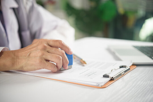 healthcare concept showing physician in white coat using rubber stamp evaluating patient prescription paperwork and authorizing medical administrative form