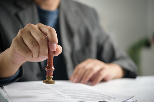 Corporate executive lifestyle showing business person using rubber stamp authorizing company paperwork evaluating legal form and official validation process