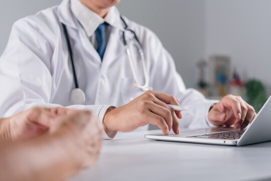 Modern medical healthcare concept showing professional physician using computer typing digital patient data while explaining treatment plan and health advice to elderly person at hospital desk