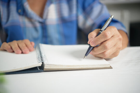 Elderly lifestyle concept showing mature person using pen writing on paper diary evaluating daily checklist making notes and organizing personal schedule at home desk