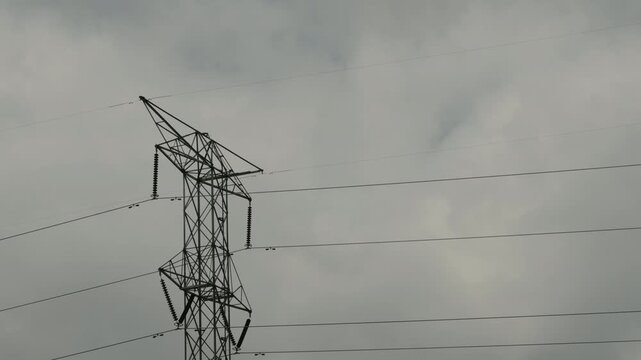 High voltage power lines tower standing against cloudy sky