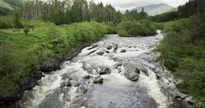 Landscape slow pan of heavy river in green forest scotland
