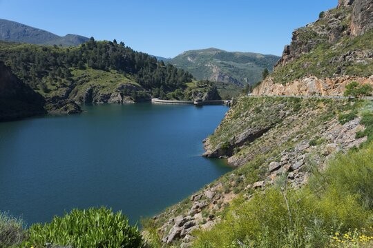 A tranquil lake in a mountainous landscape with green hills and rocks, under a clear blue sky, reservoir, Embalse de Qu&eacute;ntar, Quentar, Granada province, Andalusia, Spain