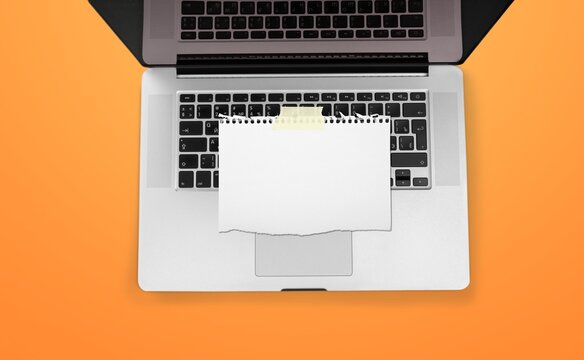 Blank torn paper note taped on a laptop keyboard over an orange background for mockup