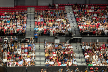 Obraz premium Blurred crowd of spectators sitting in stadium stands during large public event with shallow depth of field and abstract audience background