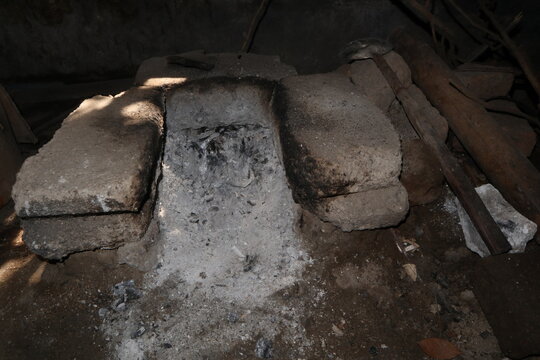 Traditional wood-fired cooking stove in a rustic rural kitchen, showing a simple clay and concrete hearth used for daily cooking with firewood.