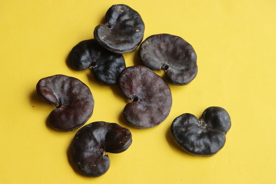 A collection of hard, dark brown Enterolobium contortisiliquum (Earpod tree) seeds, famously known for their distinct ear-like or kidney-shaped appearance. The textured botanical specimens are scatter