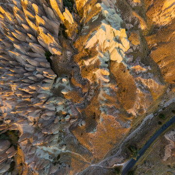Goreme, Nevsehir, Turkey. Devrent Valley fairy chimneys and mushroom-shaped volcanic rock pillars, glowing in warm golden hour light, top-down aerial view over the eroded landscape