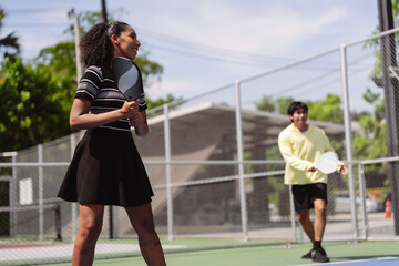 Naklejka premium Pickleball doubles team partners ready for outdoor court match game. Smiling active woman holding paddle waiting to play fitness sports.