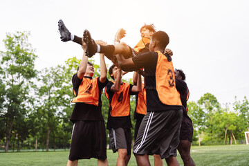 Fototapeta premium Diverse soccer players lifting their teammate up in celebration. Teamwork, victory and success concept during a football match.