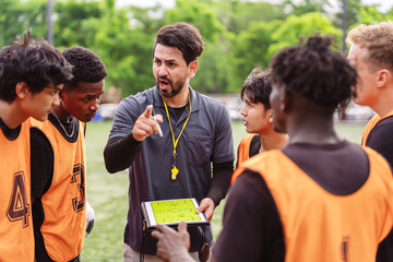 Coach pointing and explaining strategy to soccer players on the field. Teamwork, planning, and professional leadership concept in sports. © Kiattisak